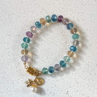 One of a kind rainbow fluorite bracelet with gold celestial charms displayed on white marble surface - handcrafted gemstone jewelry