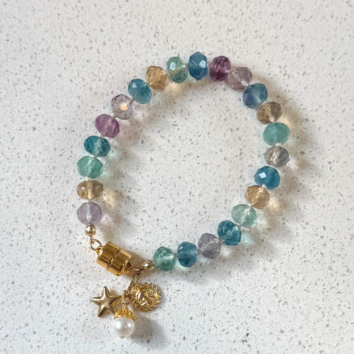 One of a kind rainbow fluorite bracelet with gold celestial charms displayed on white marble surface - handcrafted gemstone jewelry