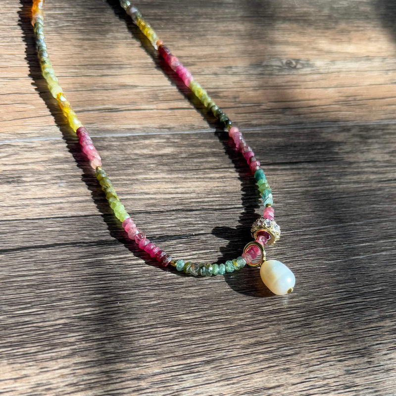 Close-up detail of Riviera Romance choker showing colorful tourmaline beads in pink, green, yellow and blue with gold accents and pearl drop pendant on rustic wooden surface