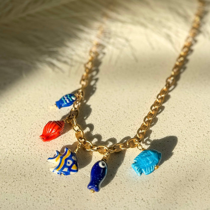 Close up detail of under the sea charm necklace featuring blue, red and yellow tropical fish charms on gold chain - handmade ocean jewelry