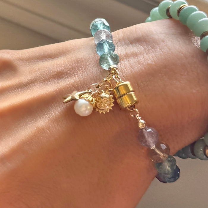 Close up detail of gold filled star sun and pearl charms on rainbow fluorite bracelet worn on woman’s wrist