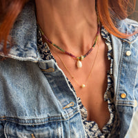 Woman wearing Riviera Romance tourmaline choker necklace layered with gold chains over denim jacket, showing how to style gemstone choker jewelry for casual chic look