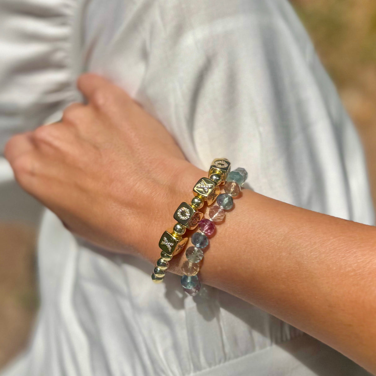 Woman wearing rainbow fluorite bracelet stacked with gold beaded bracelet showing layered jewelry styling on wrist