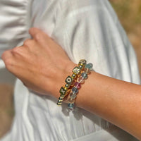 Woman wearing rainbow fluorite bracelet stacked with gold beaded bracelet showing layered jewelry styling on wrist