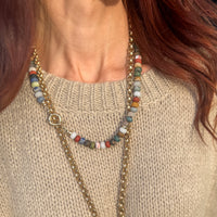 Terra Tapestry necklace worn layered with gold chain against cream sweater showing multicolored matte gemstone beads