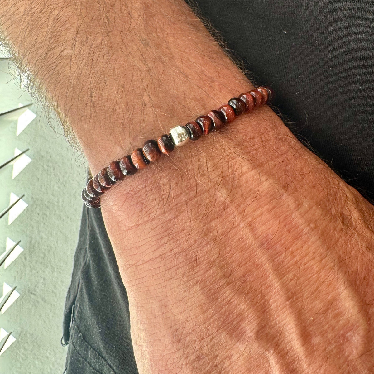 Man’s tiger eye bracelet with red beads on a wrist against a neutral backgrounds 