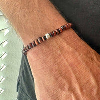 Man’s tiger eye bracelet with red beads on a wrist against a neutral backgrounds 